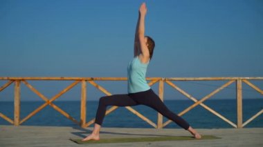 Deniz ağır çekim yakınındaki bir ahşap zemin üzerinde yoga yaparken genç ince erkek