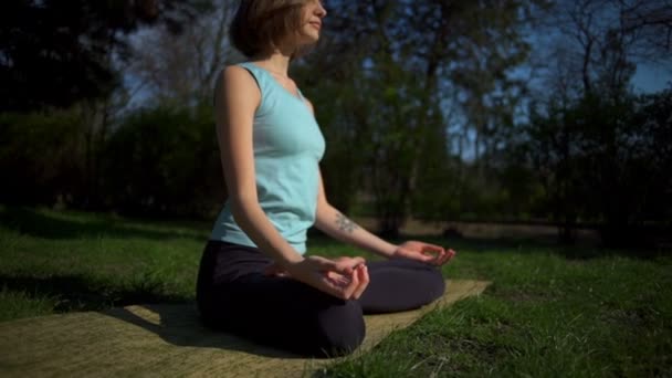 Joven hembra delgada haciendo namaste después de la pose de loto en el césped en cámara lenta parque — Vídeos de Stock