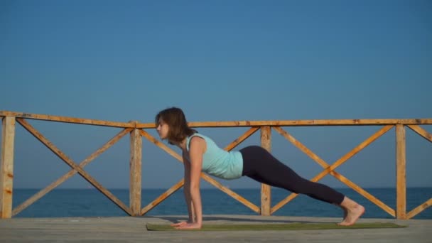 Jeune femme mince faisant pose de chien de yoga près de la mer au ralenti — Video