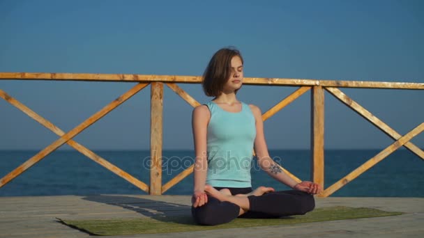 Jovem fêmea magro sentado em pose de lótus perto do mar câmera lenta — Vídeo de Stock