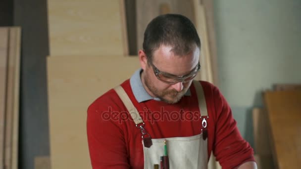 Carpintero con gafas puliendo una mesa con una lijadora eléctrica en el taller — Vídeos de Stock