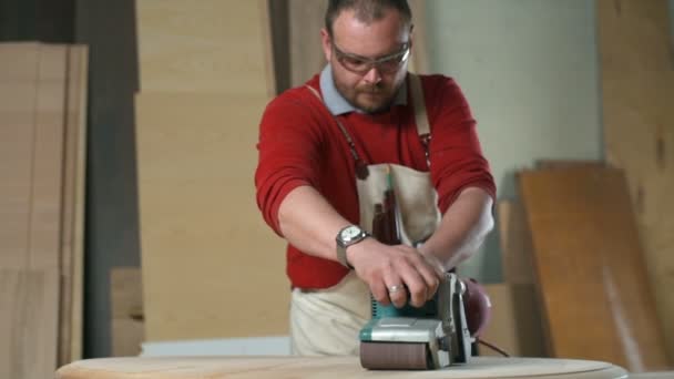 Snickare i skyddsglasögon flyttar polering maskin längs ett runt bord i en workshop — Stockvideo