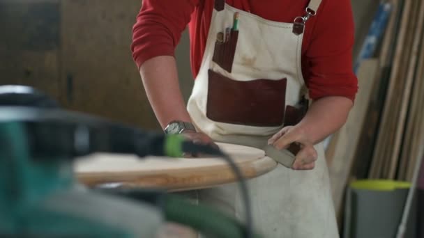 Плотник полирует край стола абразивным блоком в мастерской — стоковое видео