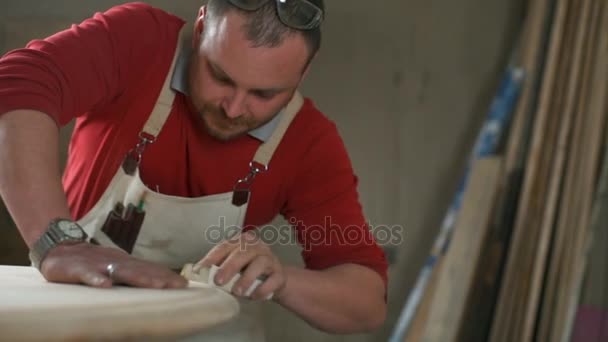 Carpenter leans on table and polishes it with abrasive block in workshop closeup — Stock Video