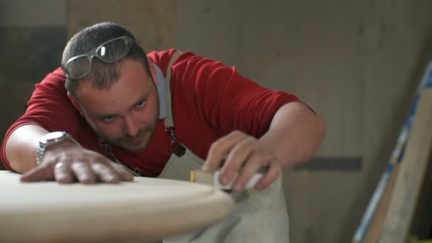 Carpenter carefully polishes an edge of table with an abrasive block in workshop — Stock Video