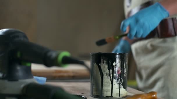 Carpintero en guantes de látex sumerge un pincel en la lata con un primer plano de tinte negro — Vídeos de Stock