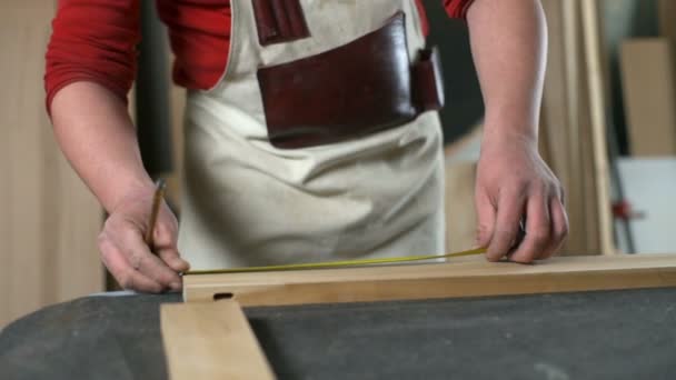Carpintero midiendo una plancha y haciendo marcas con lápiz en primer plano del taller — Vídeos de Stock