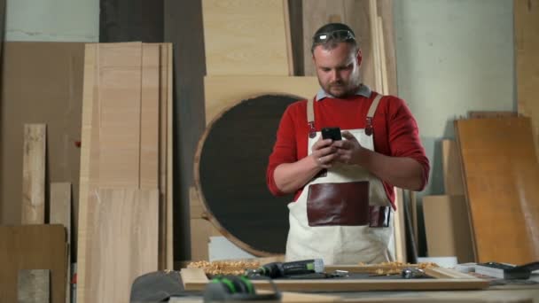 Snickare som bär en träbearbetning förkläde att skriva ett textmeddelande i en workshop — Stockvideo
