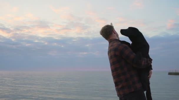 Jovem macho abraça seu cão perto do mar andar com ele câmera lenta — Vídeo de Stock
