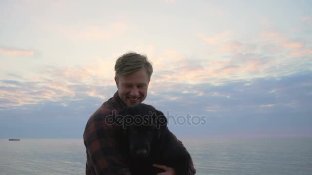 Giovane maschio tenere sulle mani il suo cane e guarda la fotocamera al rallentatore — Video Stock