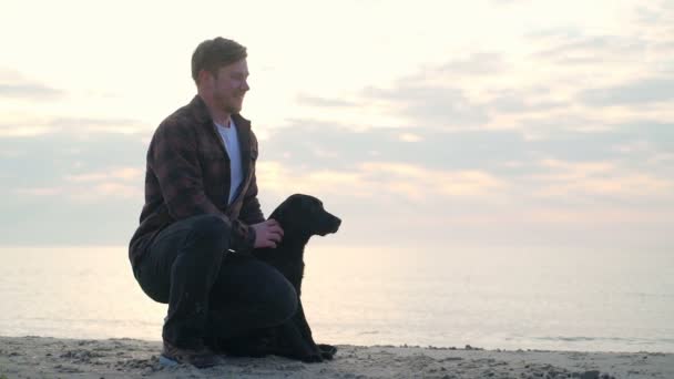 Jeune homme assis avec son chien à la mer et jouer avec lui au ralenti — Video