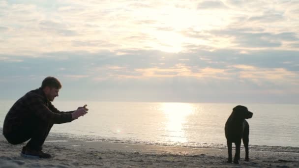 Jeune homme prend une photo ou une vidéo de son beau chien à la mer au ralenti — Video