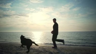 Genç erkek ile onun siyah köpek deniz yavaş hareket vasıl koşmak