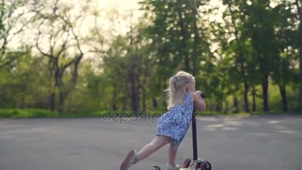 Μικρό κορίτσι Ξανθιά ιππασίας το σκούτερ της σε αργή κίνηση το πάρκο — Αρχείο Βίντεο