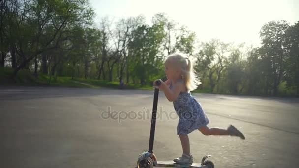 Beautiful little girl pushes herself on her scooter slow motion — Stock Video