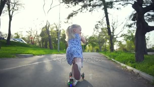 Belle jeune fille mignonne en robe chevauche son scooter dans le parc au ralenti — Video