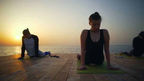 Vänner gör yoga på bryggan nära havet slow motion — Stockvideo