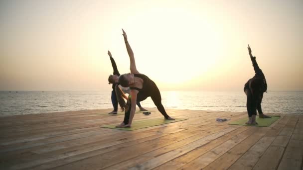 Friends doing yoga exercises on the wooden pier on the sea slow motion — Stock Video