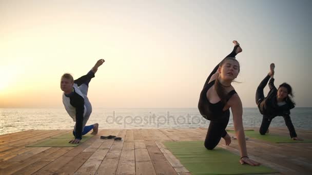 Tres personas en el muelle de madera haciendo yoga en cámara lenta — Vídeos de Stock