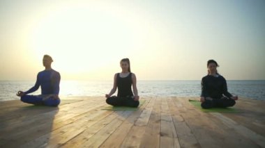 Lotus poz ahşap Teras yavaş hareket üzerinde oturan üç kişi