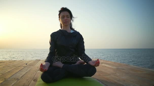 Красивая женщина сидит в позе лотоса у моря замедленной съемки — стоковое видео