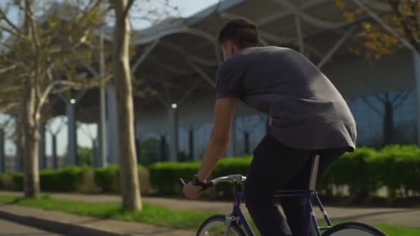 Ung man i grå skjorta och klockor rider sin cykel på gatan slow motion — Stockvideo