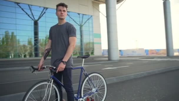 Przystojny mężczyzna stojący i trzymając jego rowerów w pobliżu lotniska w zwolnionym tempie — Wideo stockowe