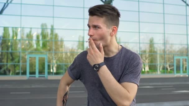 Młody mężczyzna patrząc od hotelu i palenie papierosów zwolnionym tempie — Wideo stockowe