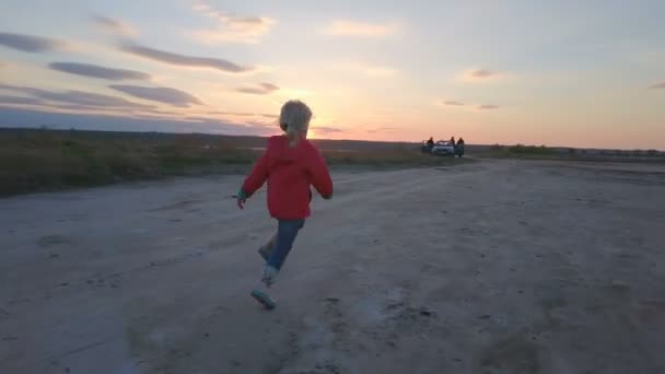 Beautiful little girl running from the drone with a sunset on the background — Stock Video