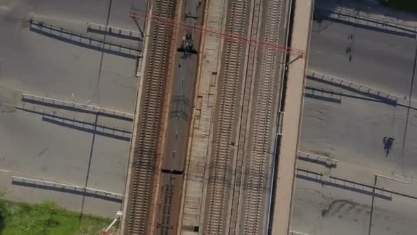 Tiro aéreo de um homem dirigindo sua bicicleta sob a ponte com um trem nele — Vídeo de Stock