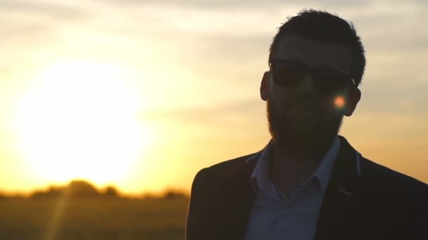 Man met een baard in glazen en een pak in het veld op zonsondergang slow motion — Stockvideo