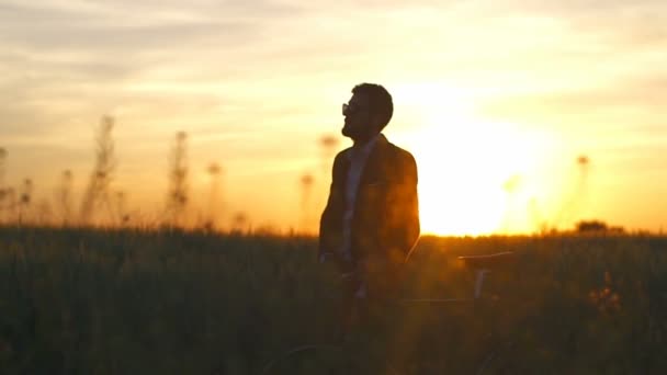 Man in de suite en glazen met een fiets in veld genieten van zonsondergang Slowmotion — Stockvideo