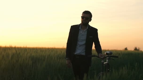 Человек в люксе и очках катается на велосипеде в поле наслаждаясь закатом замедленной съемки — стоковое видео