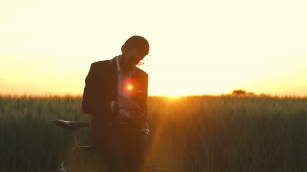 Hombre en suite y gafas de trabajo por teléfono en el campo con el amanecer bicicleta cámara lenta — Vídeos de Stock