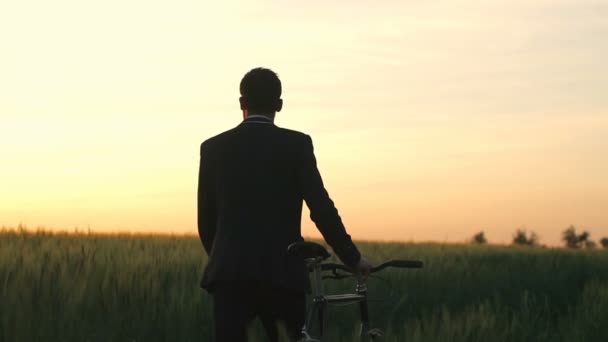 Człowiek w suite i okulary życzeń jego rower w dziedzinie piękna sundown zwolnionym tempie — Wideo stockowe