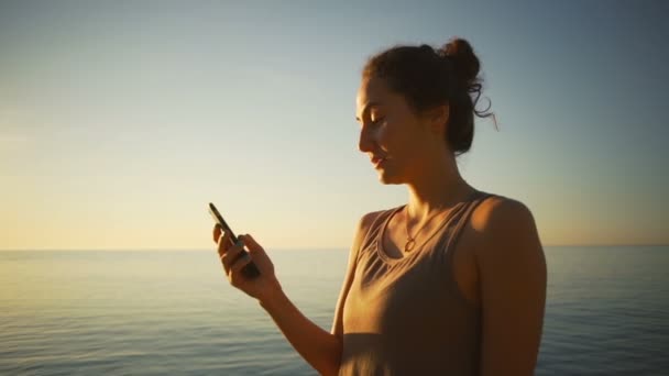 Carrera mixta hermosa mujer usando smartphone sms playa océano amanecer cámara lenta — Vídeo de stock