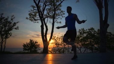 Siluet güçlü adam atlama ip değiştirmek bacaklar egzersiz açık gün batımından slowmotion