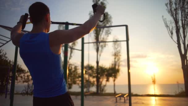 Caldo uomo forte impegnato in esercizi trx tirare su allenamento all'aperto alba rallentamento — Video Stock