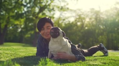 Genç güzel kız yalan çim park okşa mutlu köpek pug yaz güneşi