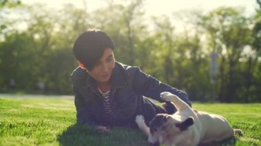 Genç kız çim park oyun okşa köpek yavrusu yatıyor mutlu yaz güneş yavaş hareket pug