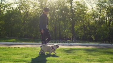 Genç gülümseyen kız yürümek köpek pug doğurmak yeşil park güneş yaz yavaş hareket ile