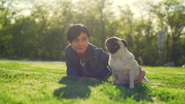 Портрет Молода дівчина лежить трав'яний парк грати пестити собаку мопс літо сонце повільний рух — стокове відео