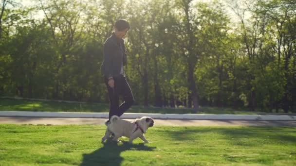 Young smiling girl walk with dog pug breed green park sun summer slow motion — Stock Video