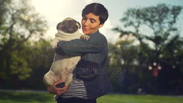 Retrato elegante chica abrazo caricia perro pug raza verde parque sol verano cámara lenta — Vídeos de Stock