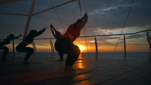 Silhouette group women practice utkatasana asana yoga class sea dawn slow motion — Stock Video