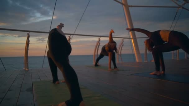 Grupo silhueta mulheres trikonasana asanas ioga classe mar amanhecer câmera lenta — Vídeo de Stock