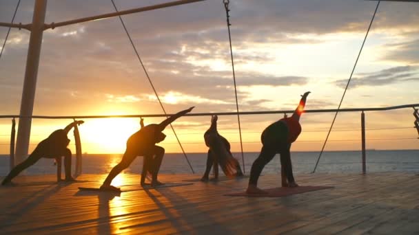 Silhouet groep vrouwen trikonasana asana's yoga klasse strand zonsopgang Slowmotion — Stockvideo