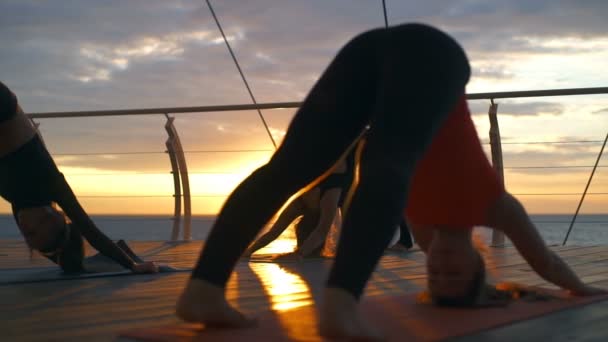 Cours de yoga jeune femme groupe pratique asana vers le bas chien coucher de soleil mer ralenti — Video