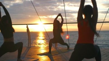 Yoga sınıf genç kadın grup uygulama asana Anjaneyasana gün batımı deniz ağır çekim
