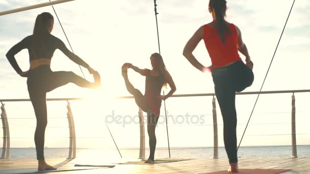 Aula de ioga jovem prática de grupo ioga asanas pôr do sol mar câmera lenta — Vídeo de Stock